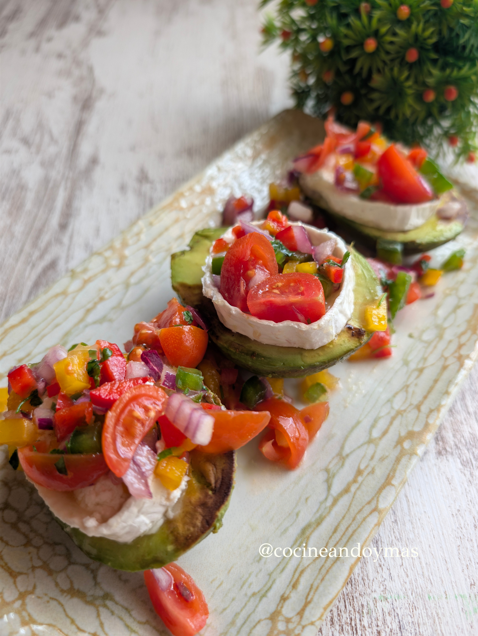 Mitades de aguacate a la plancha con queso de cabra fundido y pico de gallo de colores por encima.