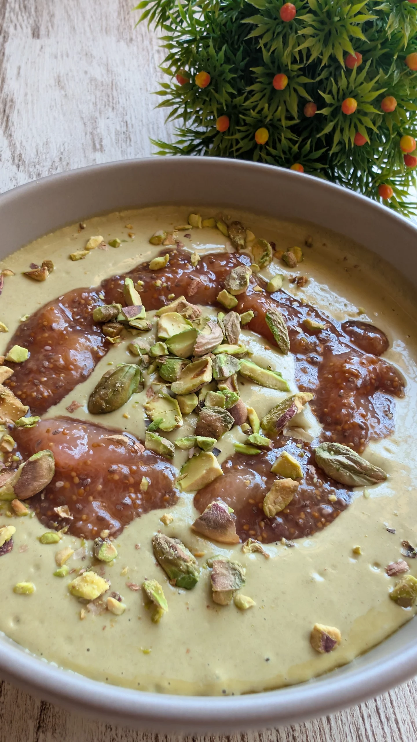 Mazamorra de pistacho servida con mermelada de higos y pistachos troceados por encima en un cuenco blanco.