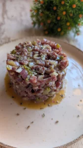 Tartar de salchichón picado con cebolla, pepinillos y alcaparras, aderezado con mostaza y soja, servido con pimienta negra.