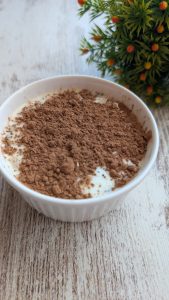Tarro de avena nocturna con capas de avena, yogur griego, cacao y cacahuete, decorado con polvo de cacao.