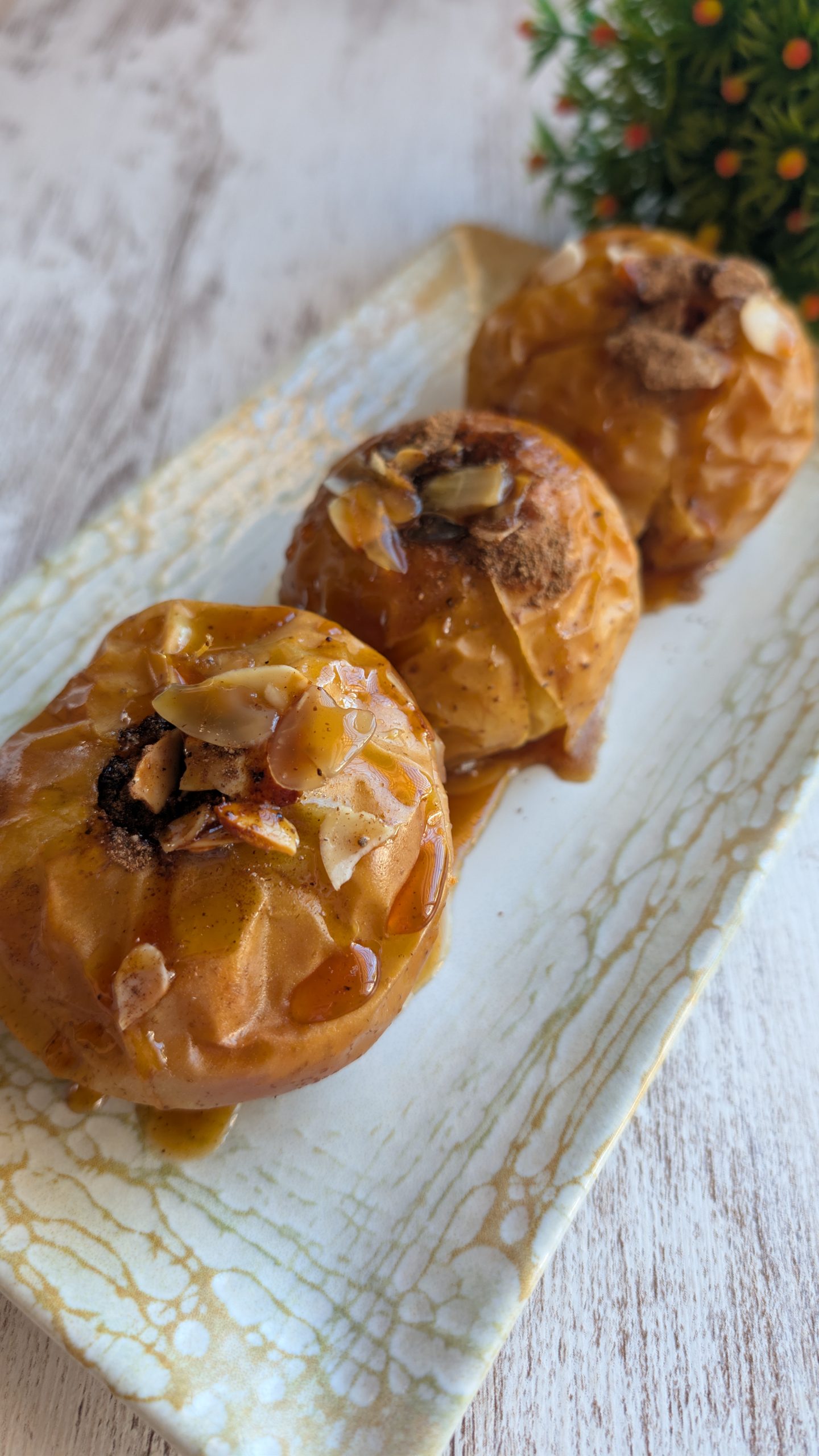 Manzanas asadas rellenas de almendras y pasas, cubiertas con miel y canela, servidas calientes.