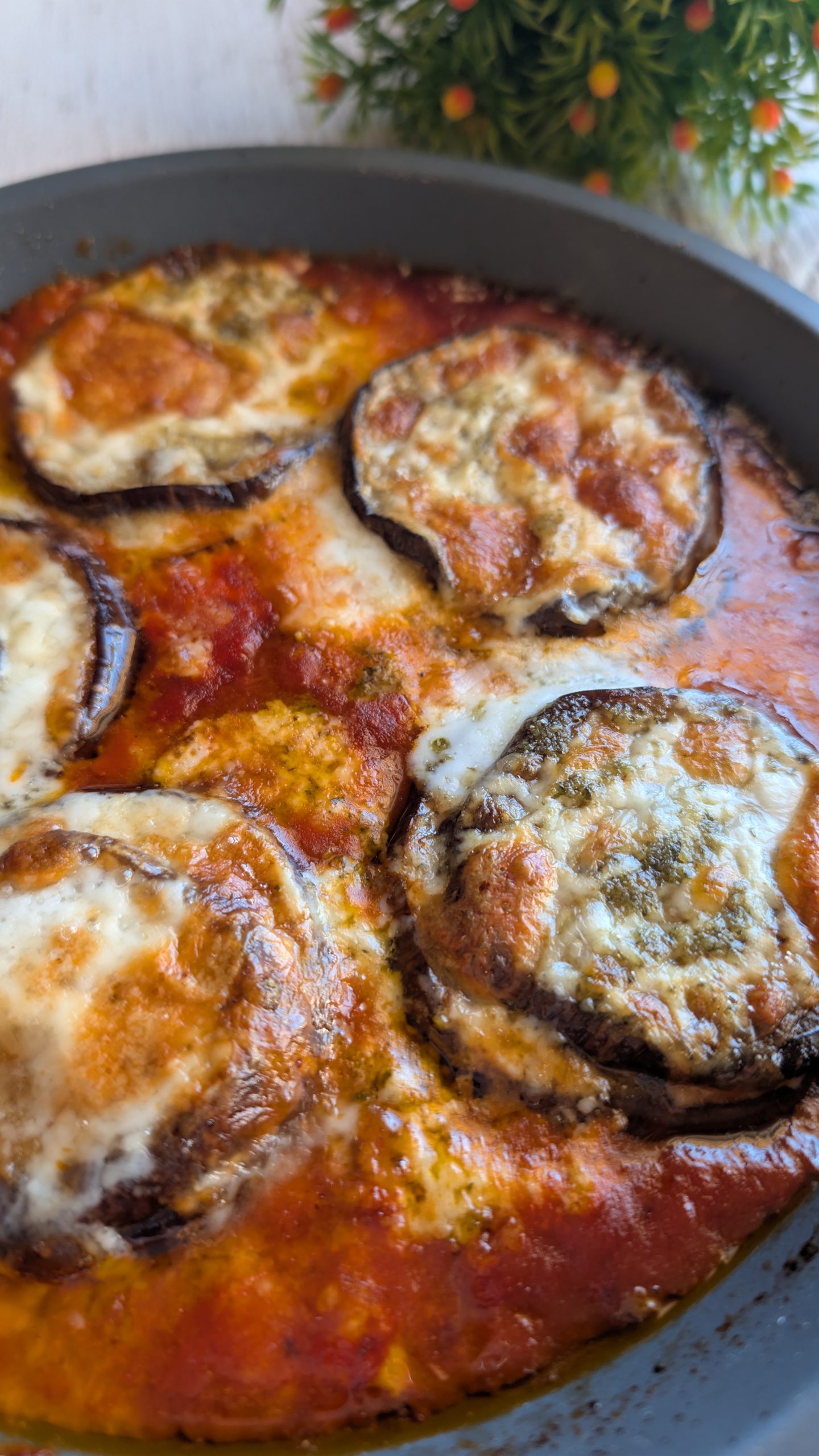 Porción de berenjenas gratinadas con pesto, queso derretido y salsa de tomate en una fuente de horno
