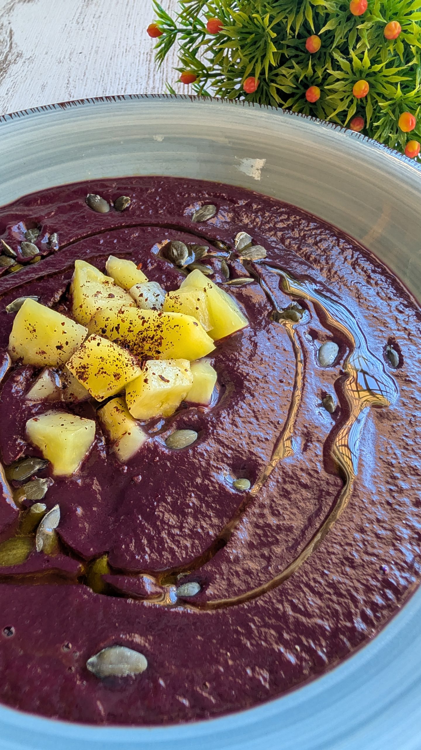 Puré de zanahoria morada servido en un tazón con topping de dados de patata, pipas de calabaza y zumaque