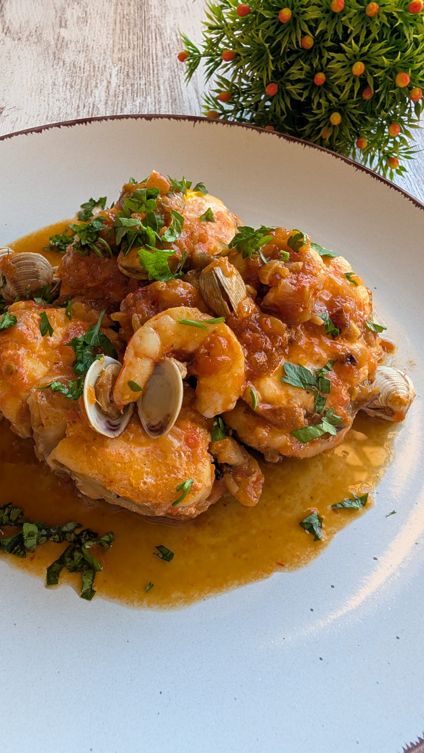 Plato de rape en salsa roja con gambas peladas y almejas abiertas, decorado con perejil fresco picado