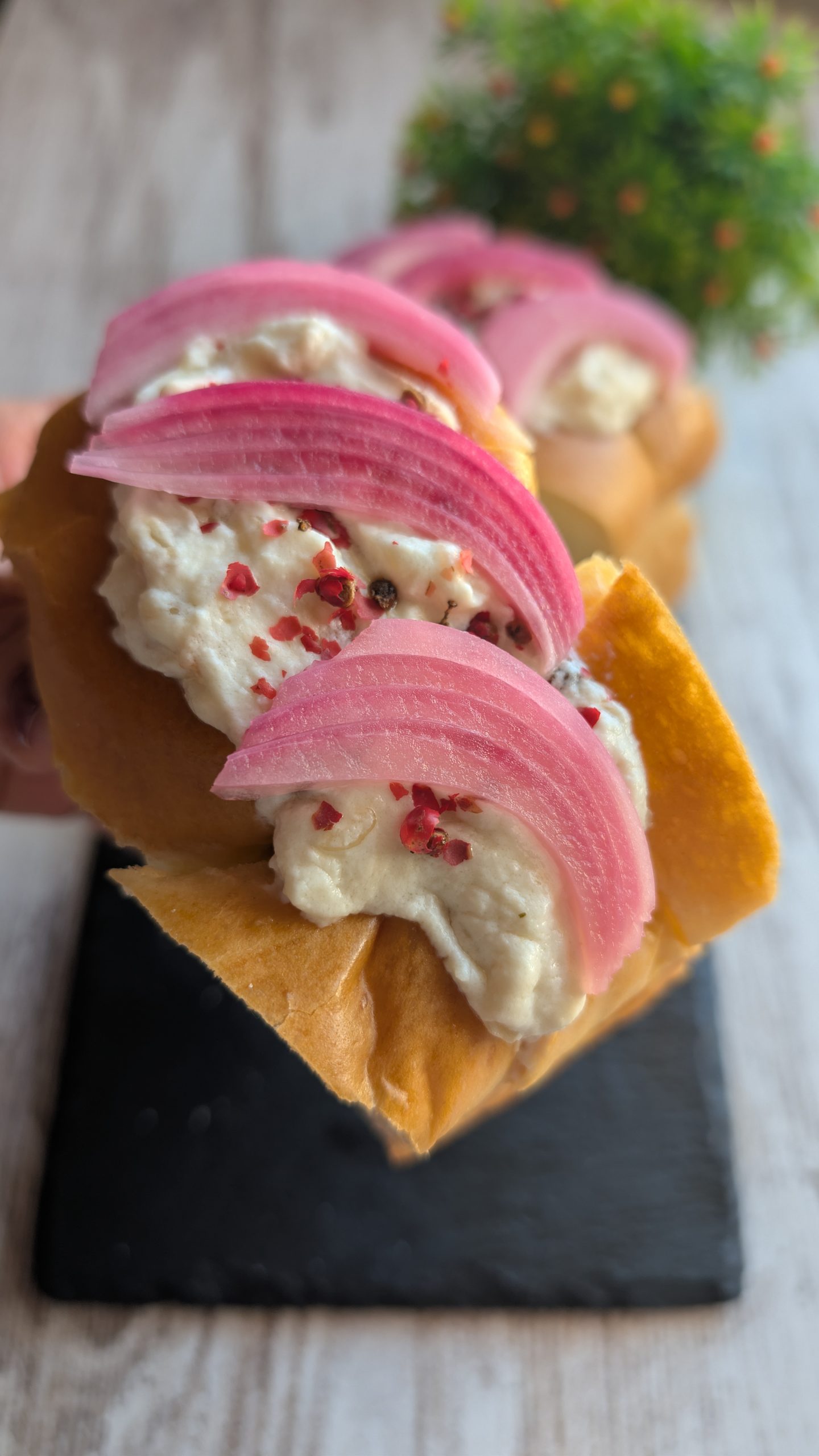 Mini pan brioche relleno de rabo de toro desmenuzado, salsa de queso cremoso y cebolla encurtida con pimienta rosa.