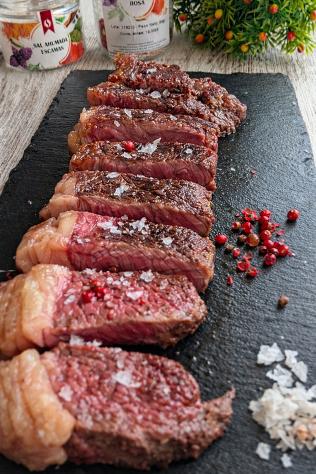 Entrecot de vaca sellado a la plancha con cristales de sal ahumada y bayas de pimienta rosa sobre una tabla de madera.