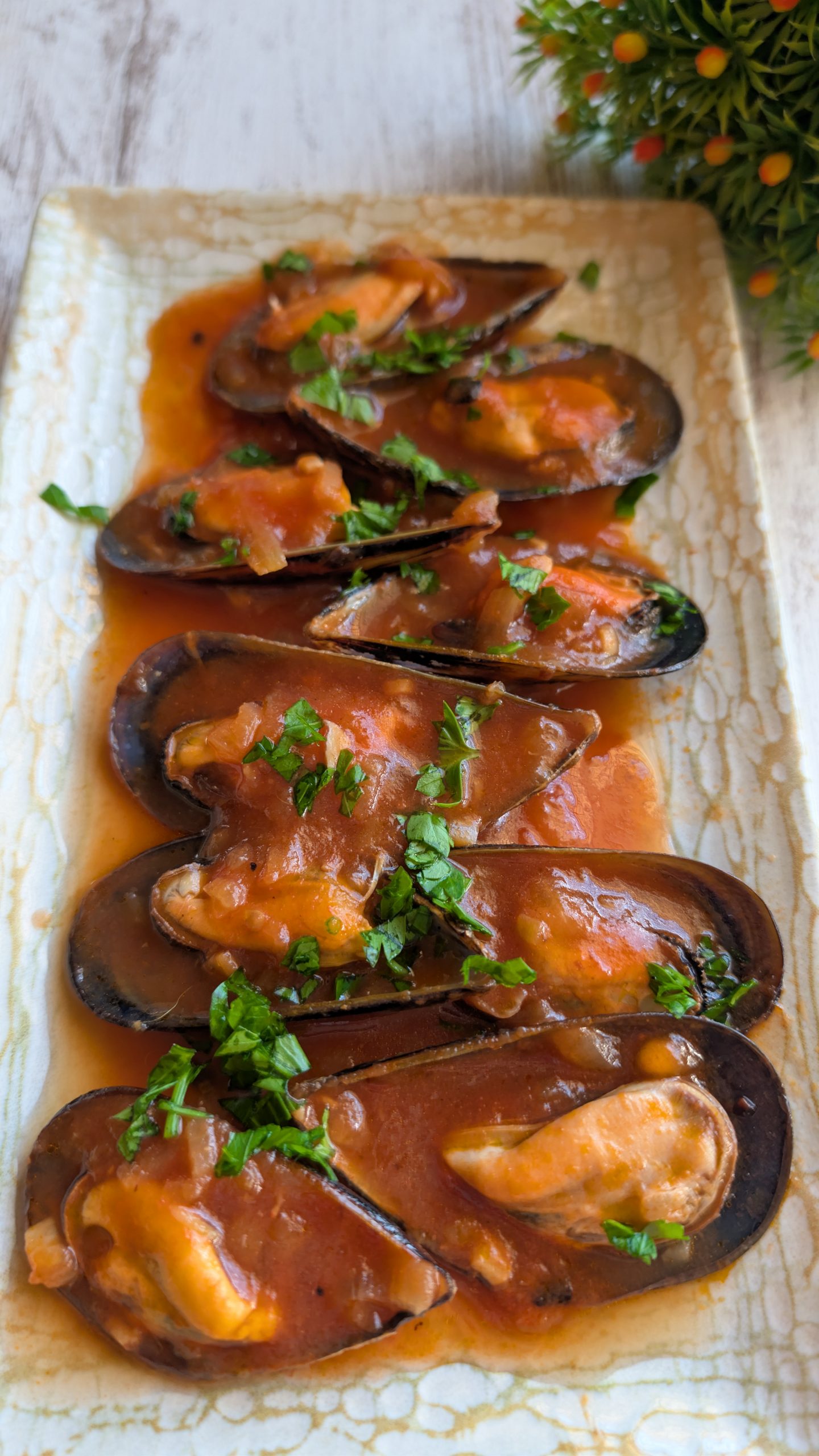 Cazuela de mejillones al vapor con salsa roja de tomate, cebolla y perejil fresco.