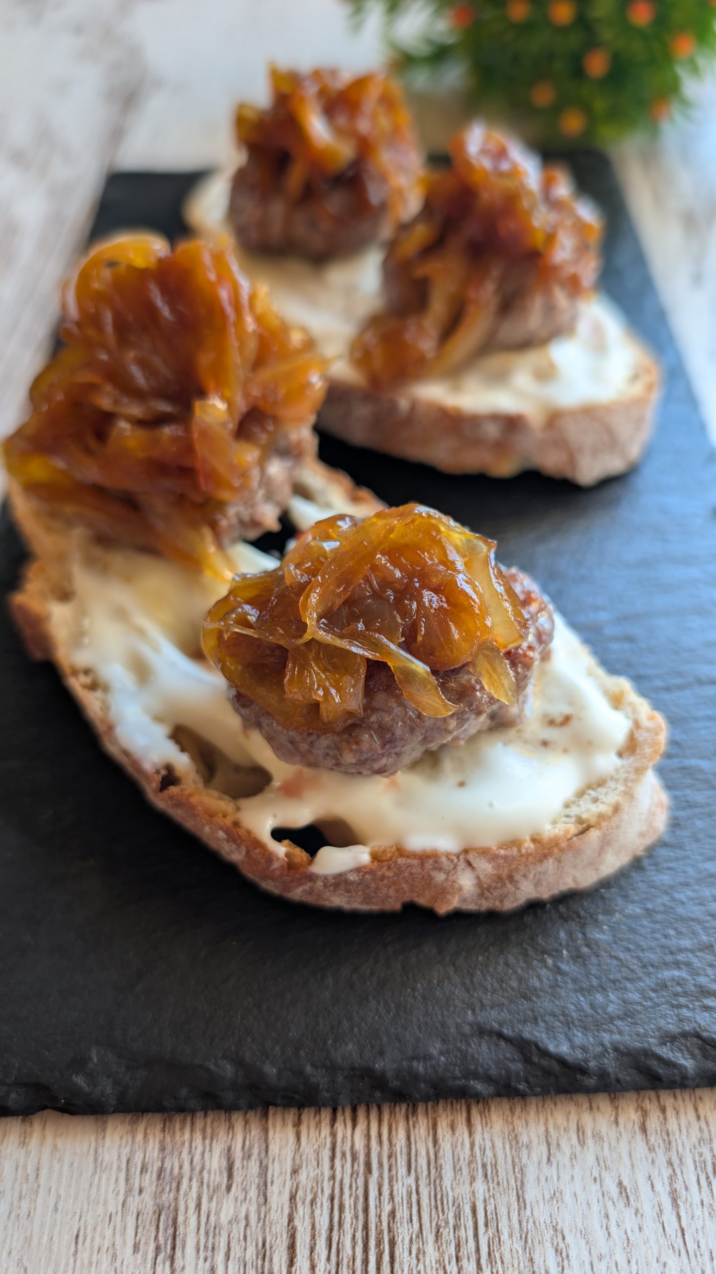 Mini hamburguesas de ternera sobre pan tostado con mayonesa y cebolla caramelizada.