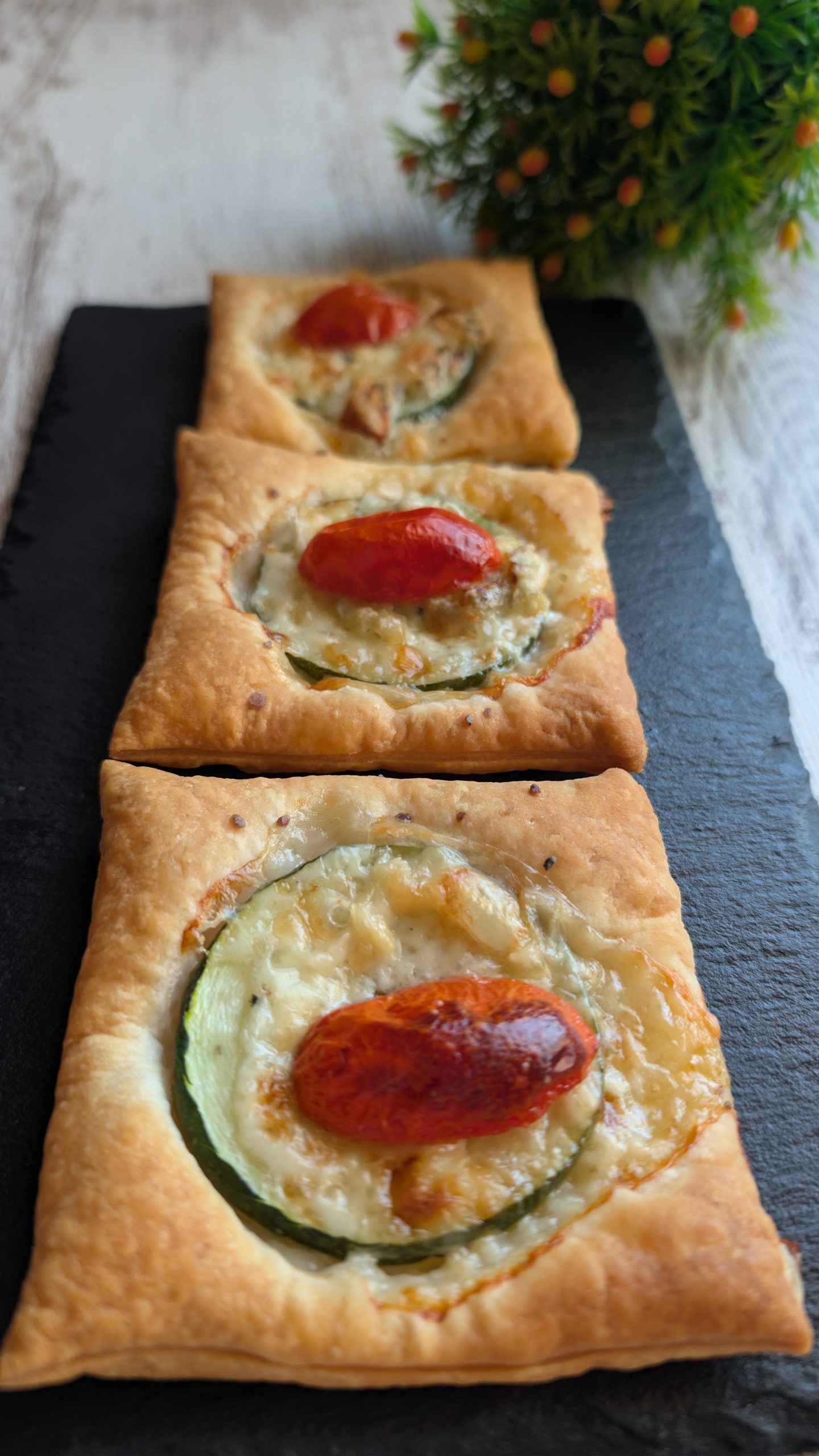 Mini hojaldres salados de calabacín y queso gorgonzola con medio tomate cherry por encima en una bandeja de horno.