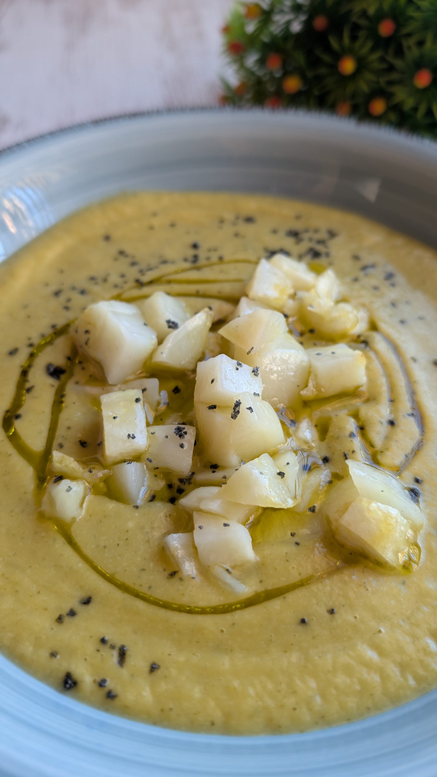 Crema de calabaza y brócoli emulsionada con aceite de oliva, servida con dados de patata y sal negra en un bol oscuro.