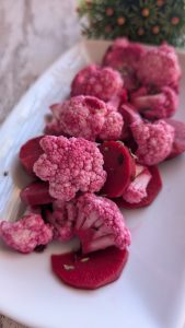 Bote de cristal con coliflor y rodajas de zanahoria morada encurtidas en vinagre con granos de pimienta.