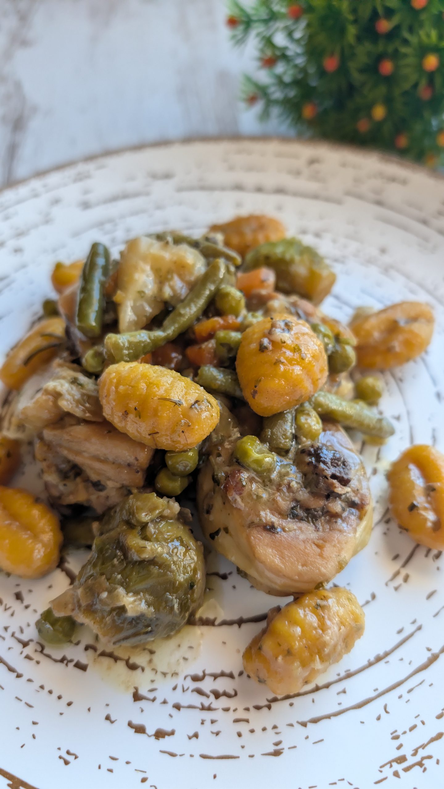 Sartén con pollo troceado al ajillo, verduras variadas y ñoquis de patata en una salsa espesa con hierbas aromáticas.