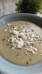 Bol de crema de puerros blanca decorada con trozos de queso, pimienta y un hilo de aceite de trufa.