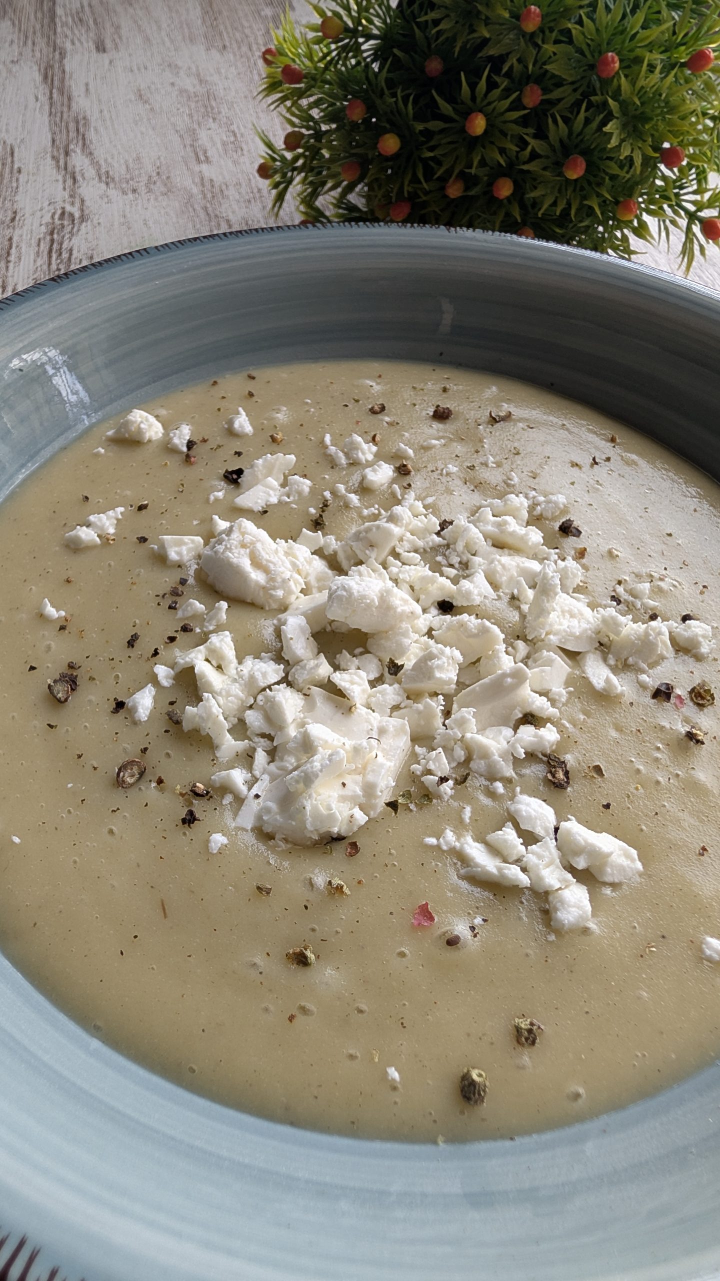 Bol de crema de puerros blanca decorada con trozos de queso, pimienta y un hilo de aceite de trufa.