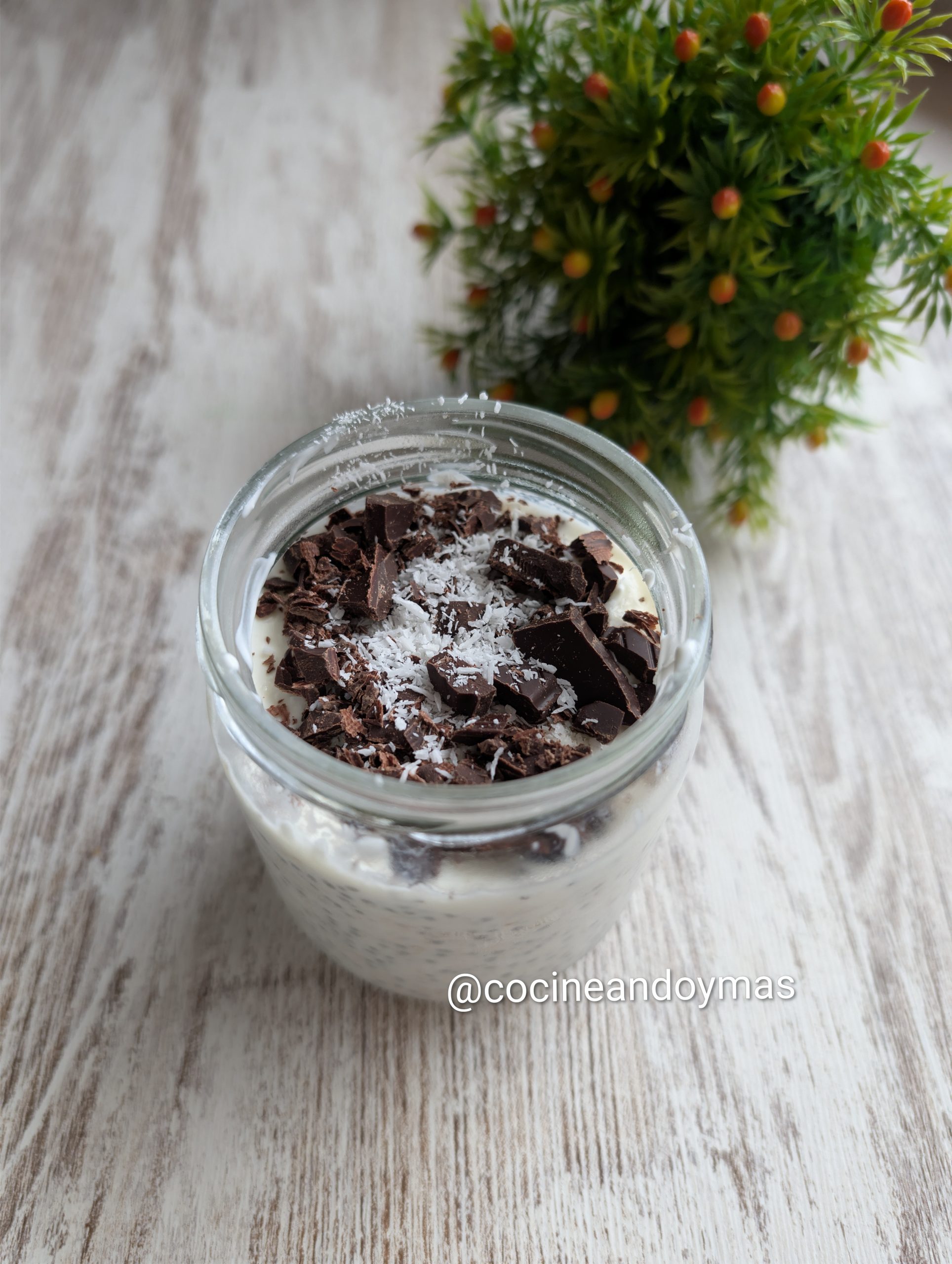 Tarro de cristal con avena nocturna (overnight oats) decorado con yogur griego, coco y virutas de chocolate.