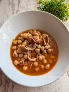 Plato de cuchara con garbanzos tiernos y calamares troceados en un sofrito de verduras espeso y rojizo.