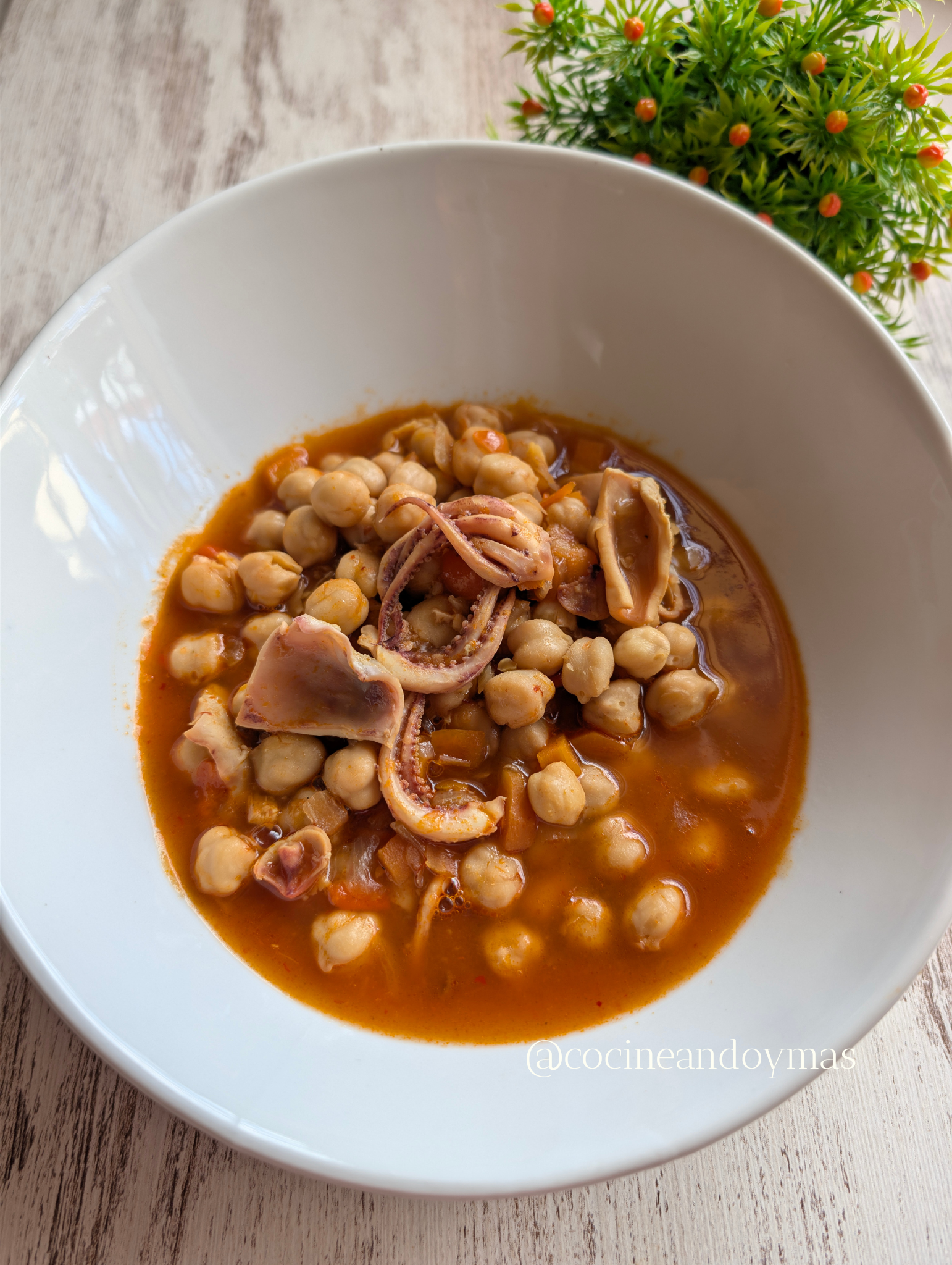 Plato de cuchara con garbanzos tiernos y calamares troceados en un sofrito de verduras espeso y rojizo.