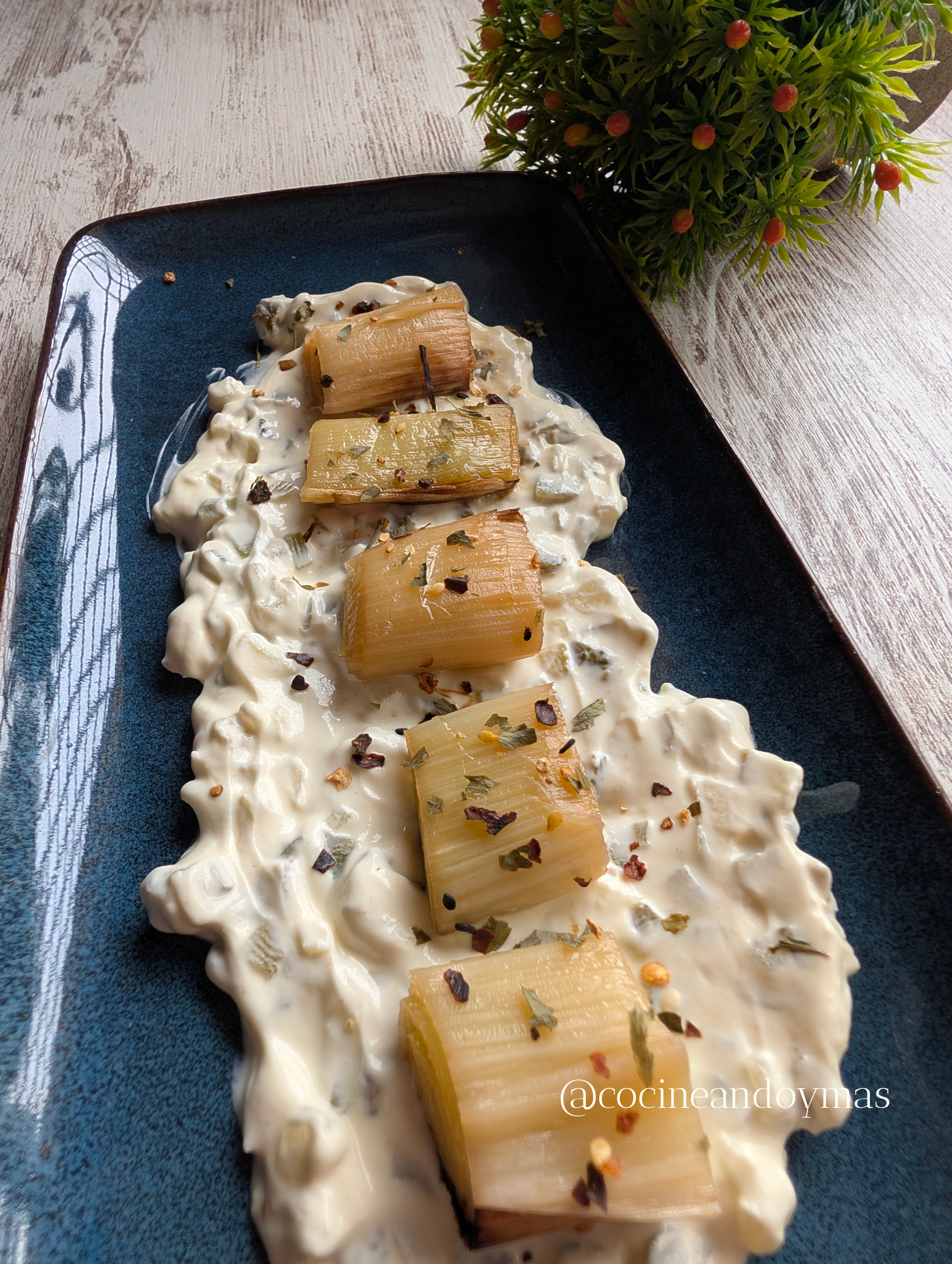 Puerros asados dorados servidos sobre una base de salsa de yogur cremosa en un plato blanco.