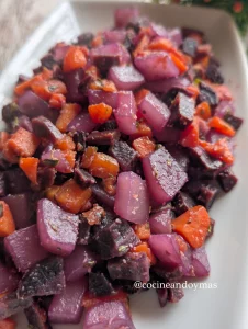 Dados de patata teñidos de morado y zanahorias salteadas con especias en una sartén con aceite de oliva.