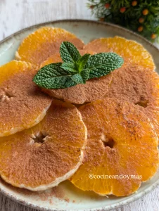 Rodajas de naranja fresca espolvoreadas con canela y un hilo de aceite de oliva sobre un plato de cerámica.