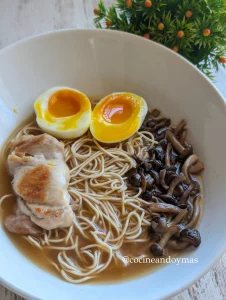 Cuenco de ramen con caldo cremoso de cacahuete y miso, acompañado de huevo con yema líquida, pollo y setas.