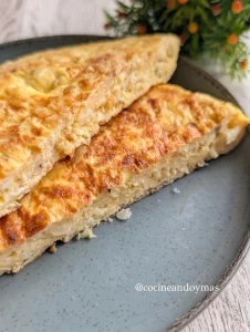 Tortilla redonda y dorada hecha con coliflor rallada y queso fundido en un plato blanco.