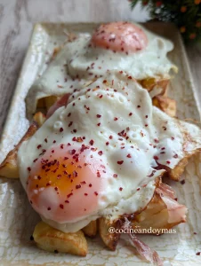 Plato de patatas doradas en airfryer con huevos a la plancha de yema líquida, láminas de jamón y escamas de pimentón.