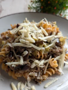 Plato de pasta de lentejas rojas y guisantes con trozos de berenjena salteada, atún y queso rallado por encima.