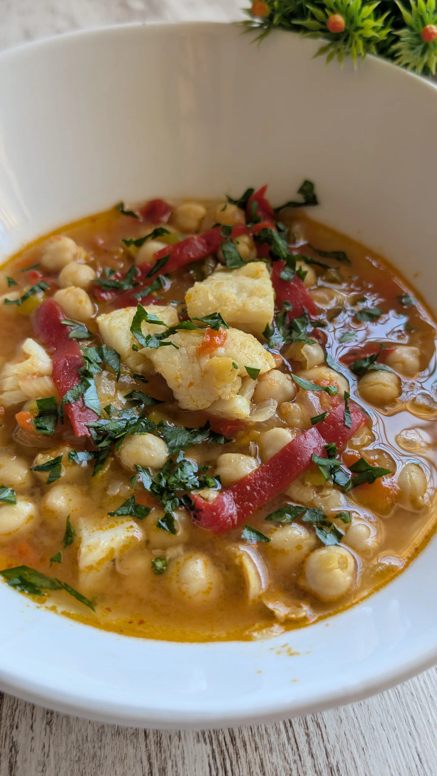 Plato hondo de potaje de garbanzos con lascas de bacalao jugoso, tiras de pimiento del piquillo y un caldo espeso de color dorado.