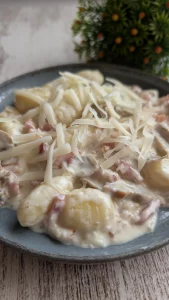 Plato de ñoquis de patata bañados en salsa carbonara cremosa con láminas de champiñones, bacon crujiente y queso rallado por encima.