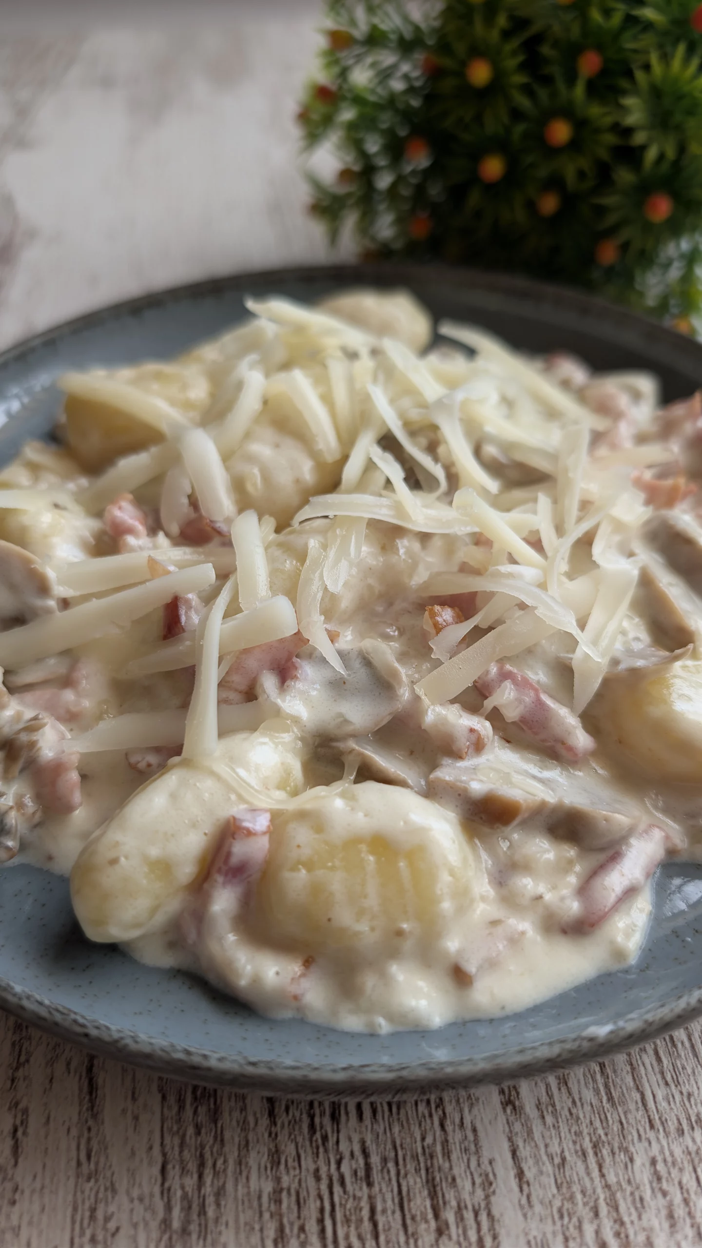 Plato de ñoquis de patata bañados en salsa carbonara cremosa con láminas de champiñones, bacon crujiente y queso rallado por encima.