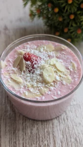Vasitos de cristal con crema rosa de fresa y queso cottage, decorados con láminas de almendra, coco rallado y una fresa fresca.