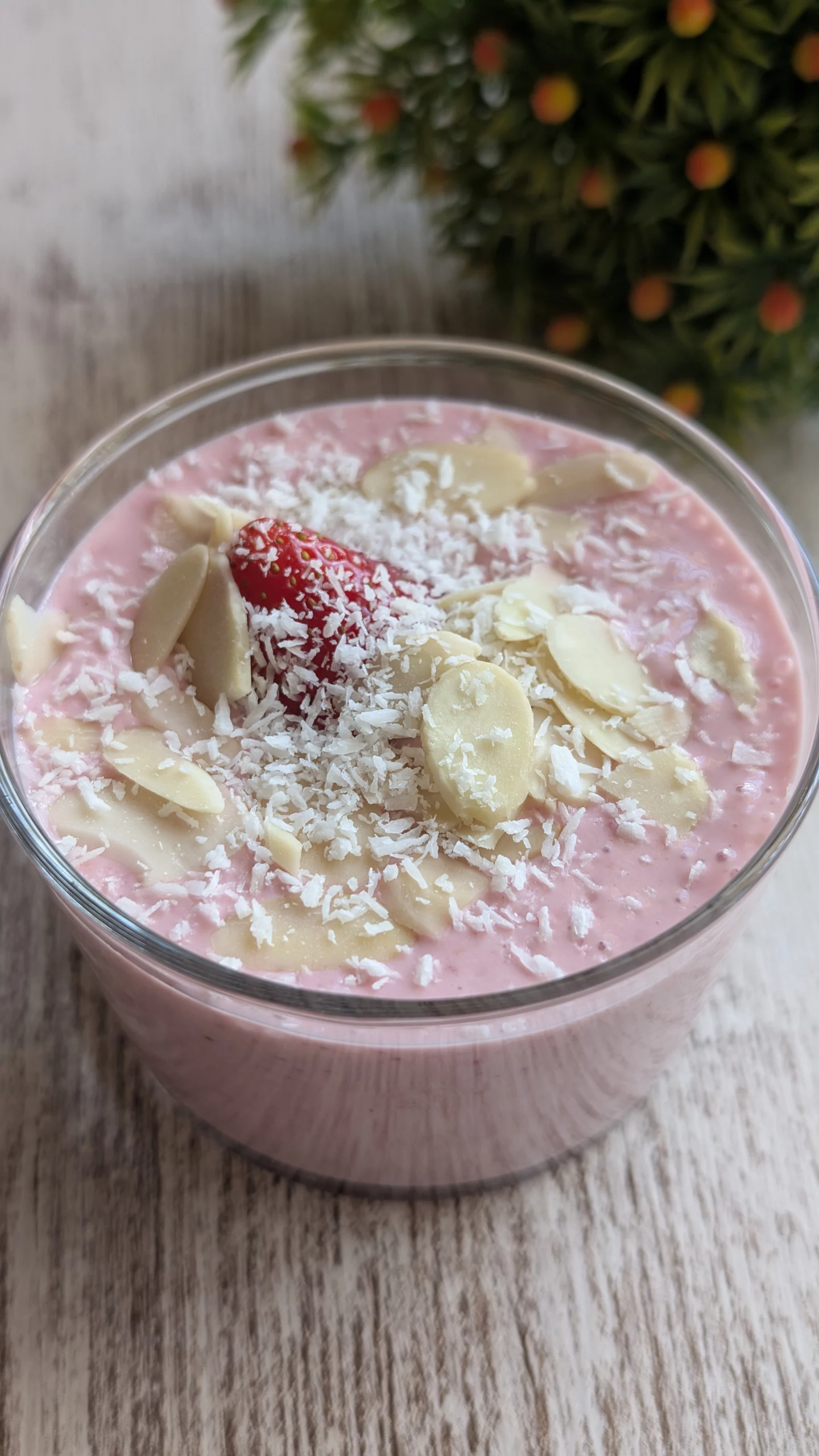 Vasitos de cristal con crema rosa de fresa y queso cottage, decorados con láminas de almendra, coco rallado y una fresa fresca.