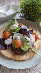 Tortilla de trigo con una capa de carne picada dorada a la plancha, cubierta con brotes verdes, tomates cherry y salsa de yogur blanco.