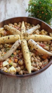 Bol colorido de ensalada de garbanzos con trozos de tomate, cebolla, pimiento, huevo cocido y atún, decorado con espárragos blancos y mazorquitas de maíz.