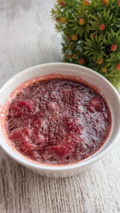 Tarro de cristal con mermelada casera de fresa espesada con semillas de chía, junto a unas fresas frescas enteras sobre la mesa.
