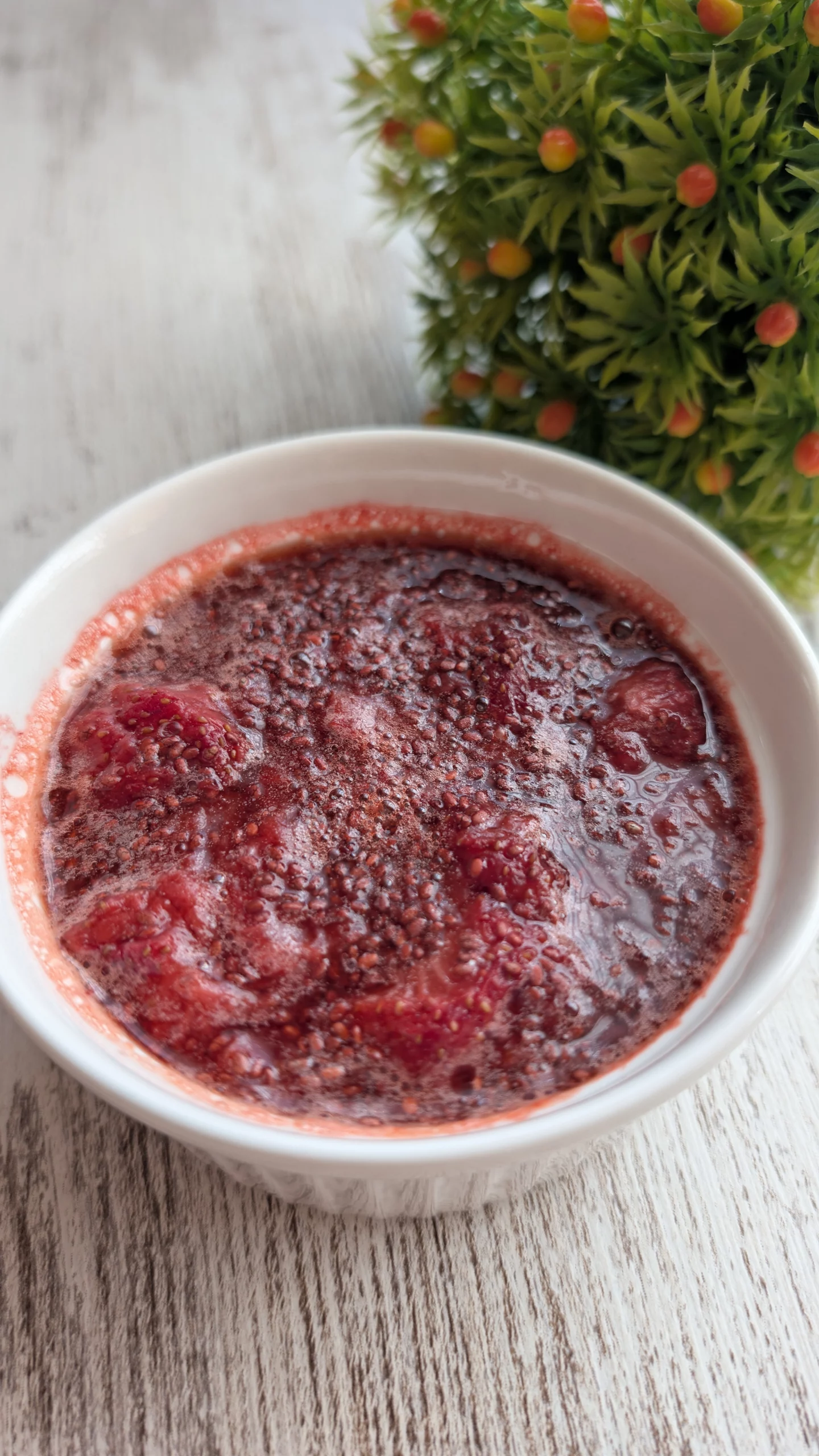 Tarro de cristal con mermelada casera de fresa espesada con semillas de chía, junto a unas fresas frescas enteras sobre la mesa.