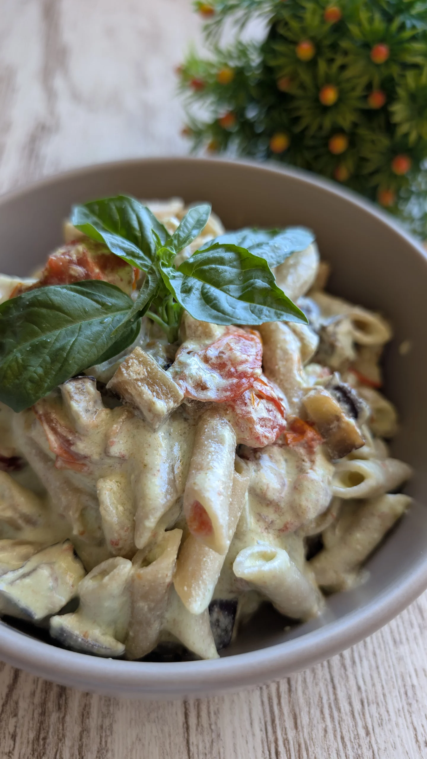 Plato de pasta mezclada con dados de berenjena asada y tomates cherry, bañada en una salsa verde cremosa de queso cottage y albahaca fresca.