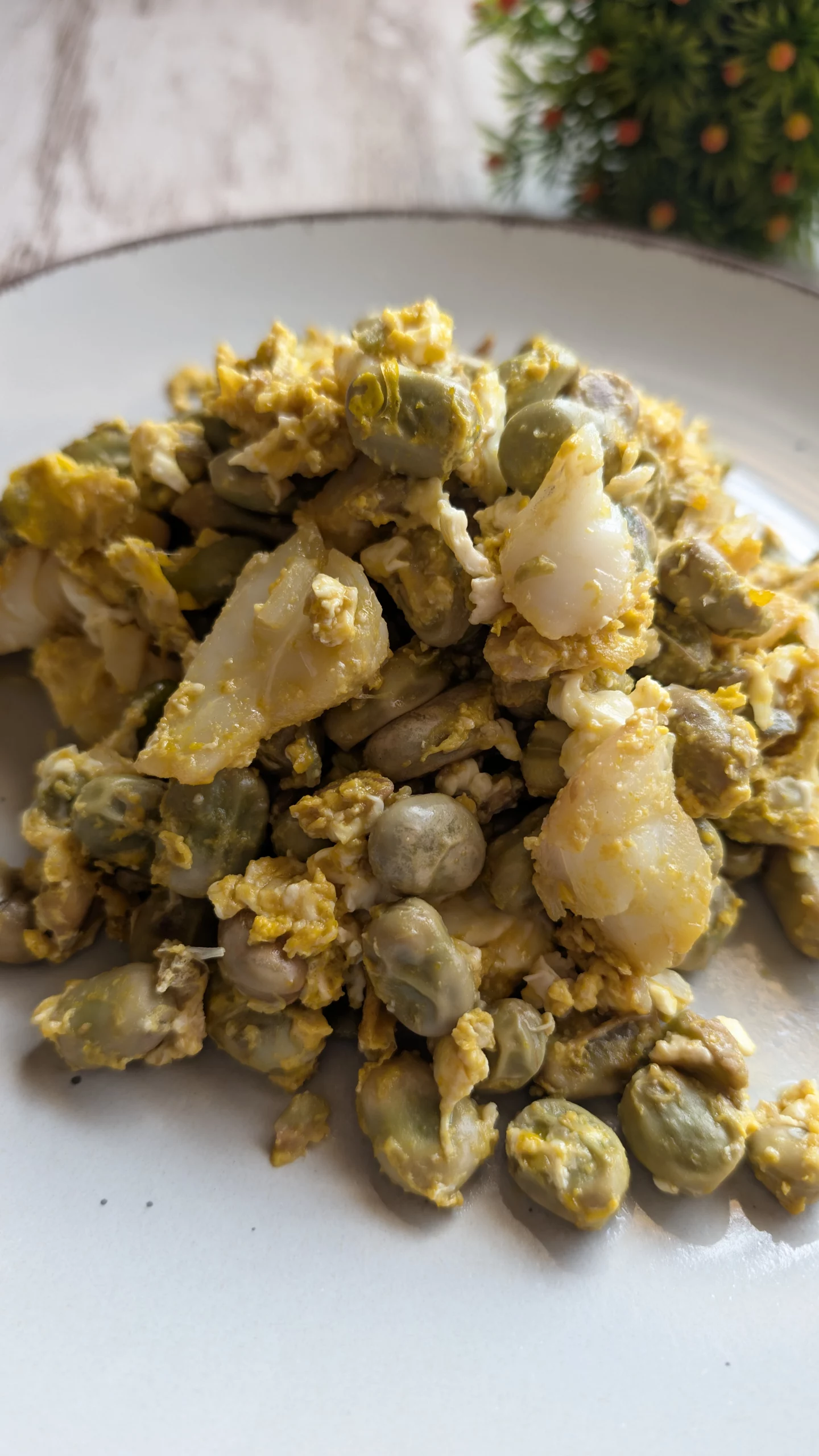 Plato hondo con un revuelto jugoso de huevo con habas verdes tiernas y lascas de bacalao desalado cocinado a la sartén.