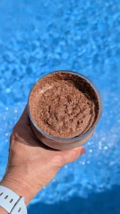 Tres vasos con batidos proteicos espumosos de color chocolate, rosa y beige, decorados con cacao, arándano en polvo y canela respectivamente.