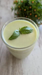 Cuenco blanco con gazpacho de melón y pepino de color verde claro, decorado con un chorrito de aceite de oliva, huevo cocido picado y hojas de albahaca fresca.