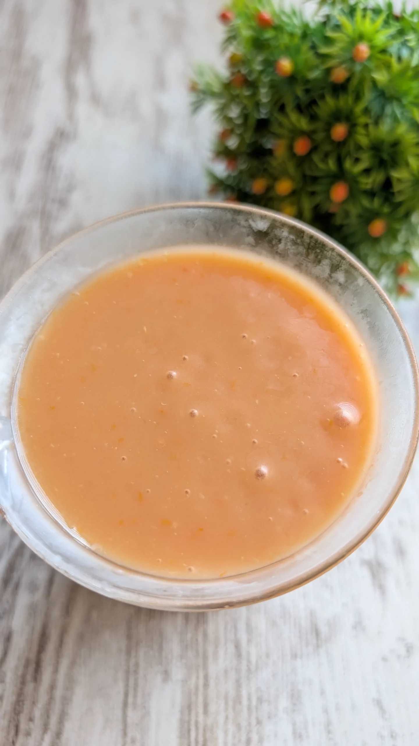 Vaso de cristal con gazpacho andaluz tradicional de color rojo anaranjado, decorado con un chorrito de aceite de oliva y brotes de albahaca.