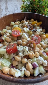 Bol con ensalada de garbanzos, dados de pepino, tomate, cebolla morada, aceitunas negras y queso feta desmenuzado con orégano.