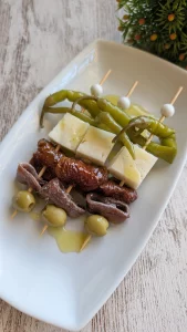 Brochetas de gilda en palillo con guindilla, queso curado, tomate seco, anchoa y aceituna verde, regadas con aceite de oliva virgen extra.