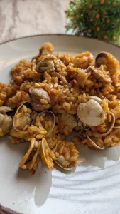 Cazuela con arroz marinero meloso decorado con almejas abiertas, gambas jugosas y trozos de calamar sobre un sofrito rojo de tomate y pimiento.
