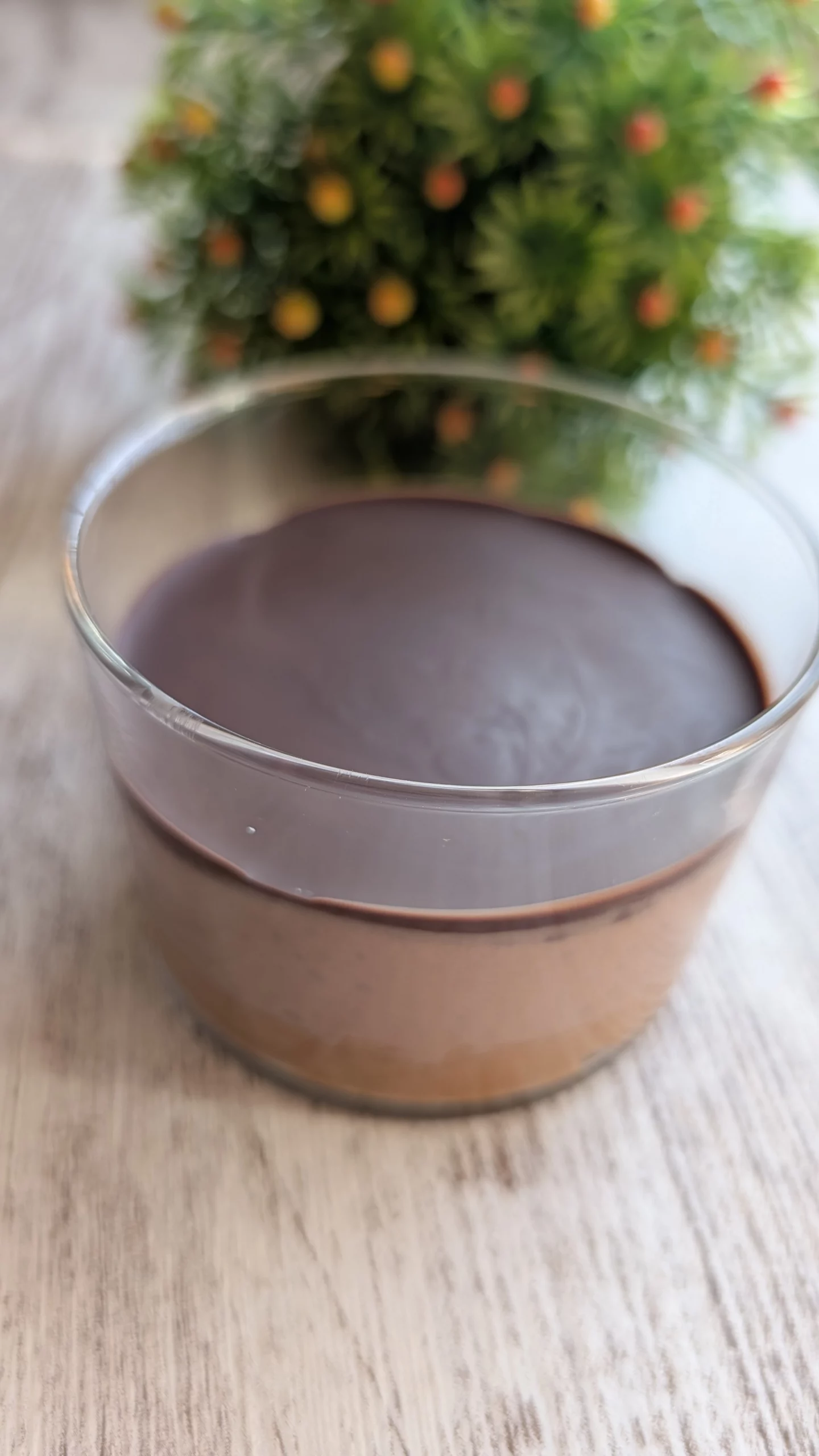 Vasito individual de cristal con capa de almendra en la base, crema de yogur y cacao en el centro y cobertura de chocolate negro crujiente quebrada por una cuchara.
