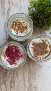 Tres tarros de cristal con avena nocturna proteica decorados con fresas frescas, cacao espolvoreado y canela de Ceylán.