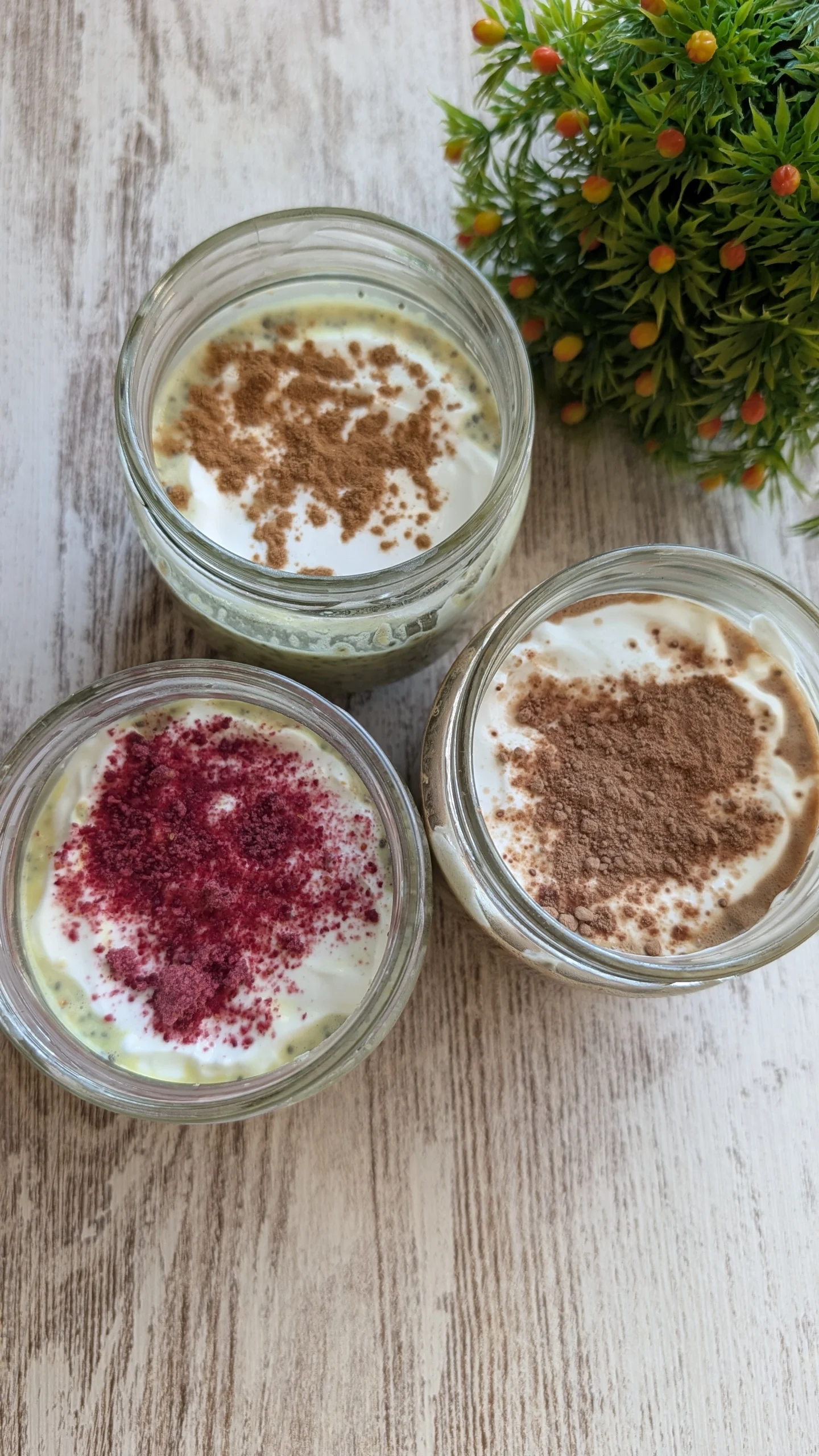 Tres tarros de cristal con avena nocturna proteica decorados con fresas frescas, cacao espolvoreado y canela de Ceylán.