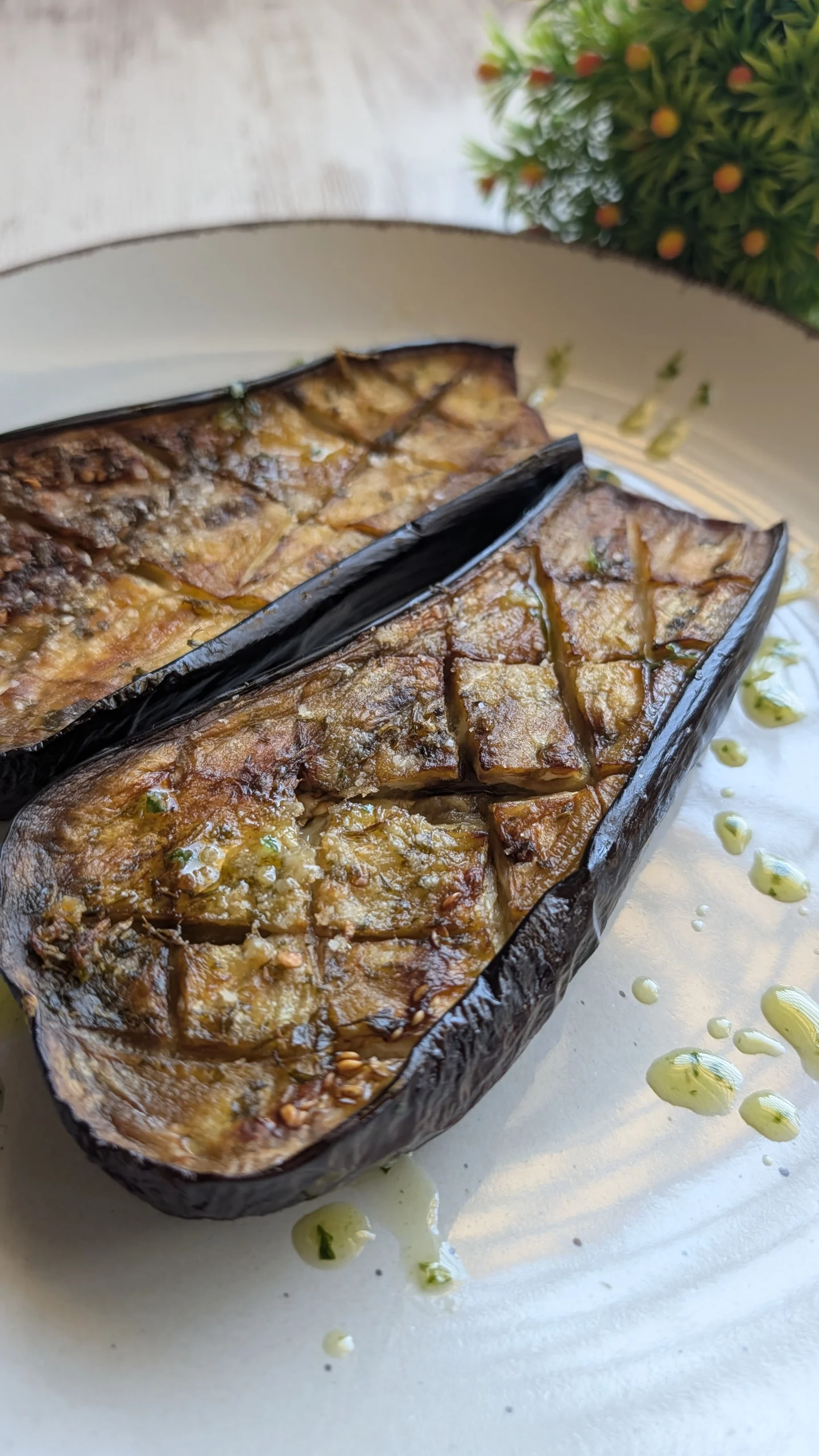 Mitades de berenjena asada al horno con rejilla en la pulpa, doradas y cubiertas de salsa verde de perejil, ajo y aceite de oliva virgen extra.