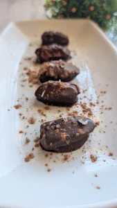 Bombones de dátil rellenos de crema de cacahuete y cubiertos de chocolate negro crujiente con escamas de sal por encima sobre papel vegetal.